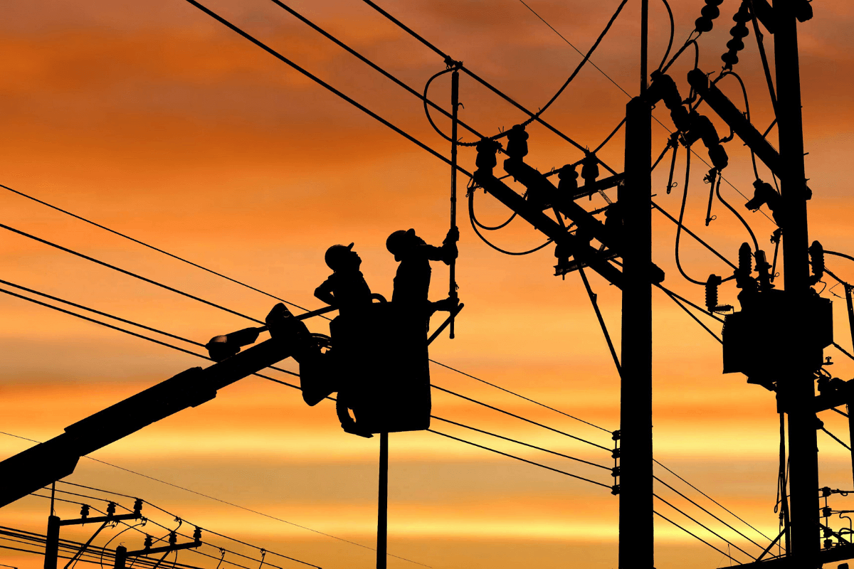 Trabalhadores realizando manutenção em linhas de transmissão elétrica durante o pôr do sol.